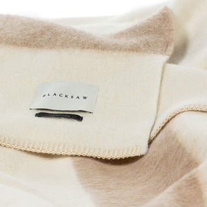 The Blacksaw 100% Recycled Siempre Blanket Blanket in  Ivory with Beige Stripe Close Up product shot showing beautiful Blacksaw brand label, Heirloom Alpaca label and Blanket Stitching detail