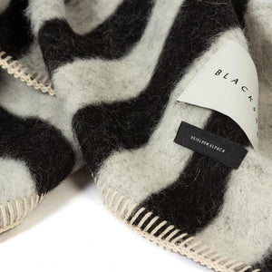 The Blacksaw Stills Vertical Stripe Blanket in  Black/Ivory Close Up product shot showing beautiful Blacksaw brand label, Heirloom Alpaca label and Blanket Stitching detail