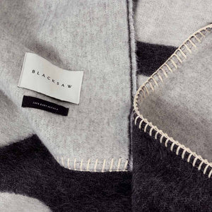 The Blacksaw  100% Alpaca, Reversible TimeWarp Throw Blanket in   Black and Ivory Close Up product shot showing beautiful brand label and Blanket Stitching detail