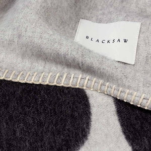 The Blacksaw  100% Alpaca, Reversible TimeWarp Throw Blanket in   Black and Ivory Close Up product shot showing beautiful brand label and Blanket Stitching detail